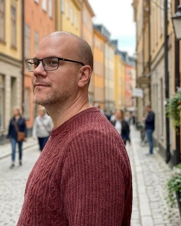 Björn Sennbrink on a cobbled street in Gamla stan, Stockholm, in glasses and a cable-knit sweater, looking to the side.