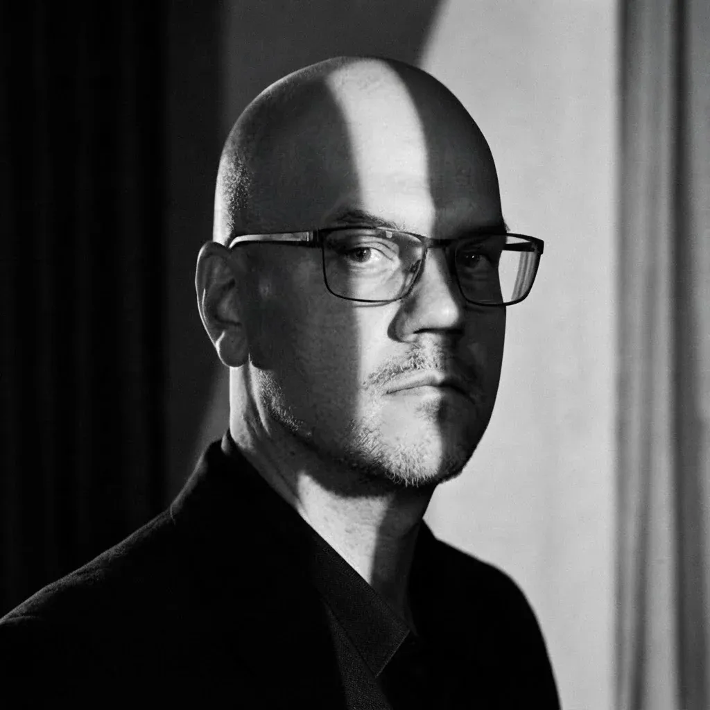 Black-and-white portrait of Björn Sennbrink in glasses and a dark jacket, half his face in shadow.